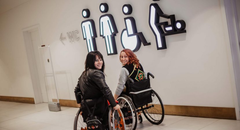 Two girls in wheelchairs near the entrance to the public toilet