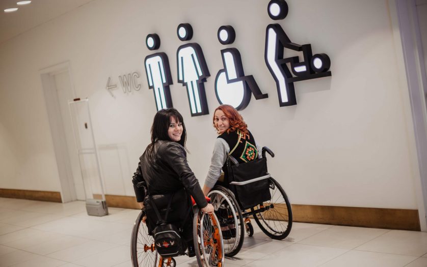 Two girls in wheelchairs near the entrance to the public toilet