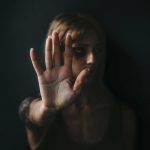 Woman raised her hand for dissuade standing against dark wall.