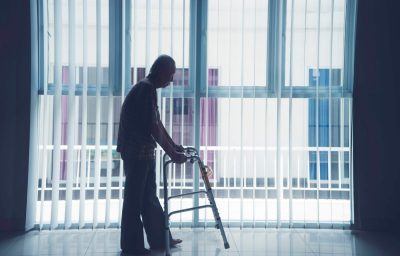 Elderly man walks with a walker near the window