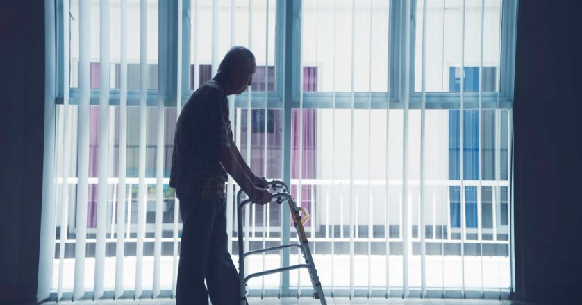 Elderly man walks with a walker near the window
