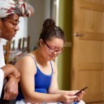 Mother with daughter with Down Syndrome looking at smart phone at home
