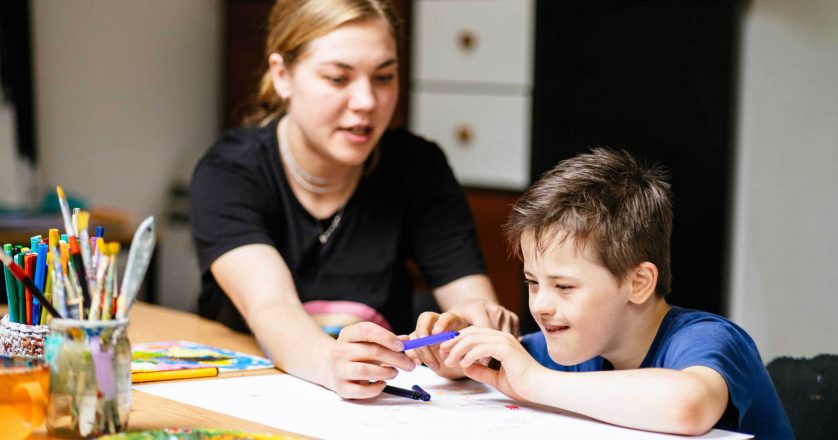 female teacher sitting at desk with a Down syndrome schoolboy