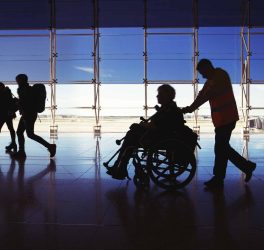 Silhouette of man in wheelchair and people carrying luggage and walking in airport