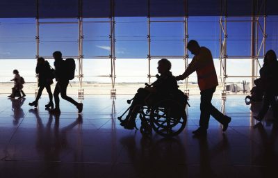 Silhouette of man in wheelchair and people carrying luggage and walking in airport