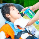 Father helping disabled son in wheelchair drink from straw cup