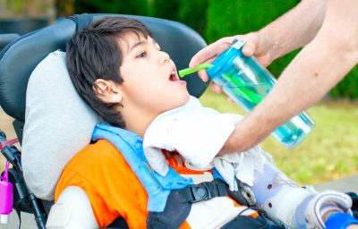 Father helping disabled son in wheelchair drink from straw cup