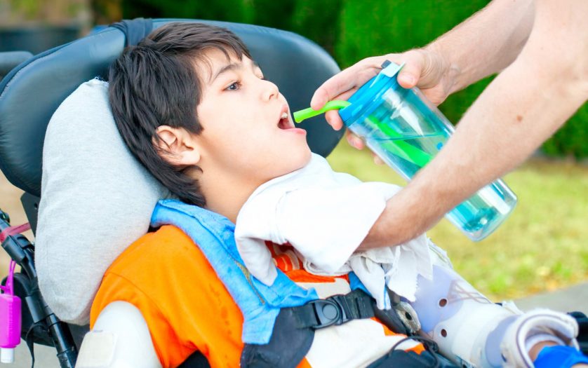 Father helping disabled son in wheelchair drink from straw cup