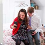 Young downs syndrome couple sitting on bed using mobile phone to take selfie at home