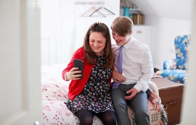 Young downs syndrome couple sitting on bed using mobile phone to take selfie at home
