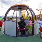 children spin an accessible playground structure with children in wheelchairs inside