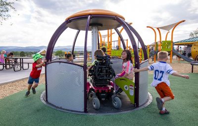 children spin an accessible playground structure with children in wheelchairs inside