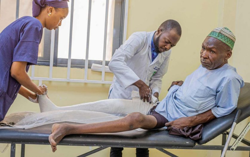 Doctor with nurse putting broken leg of old man in plaster