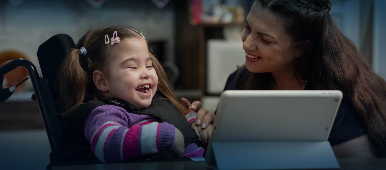 baby with disability and mother laughing and watching video online in tablet.