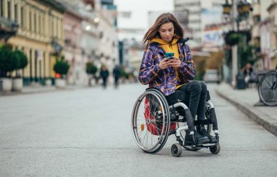 Woman in wheelchair using a smartphone while out in the city