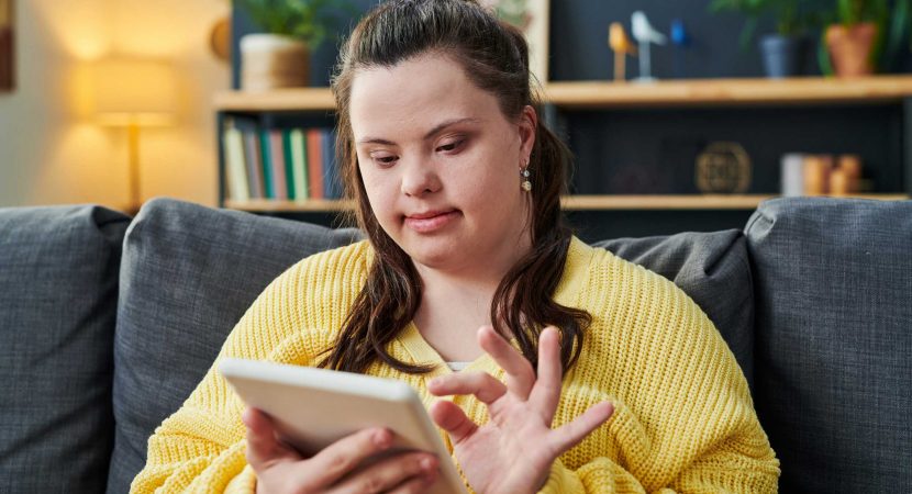Portrait of young woman with Down syndrome sitting on sofa in living room using tablet