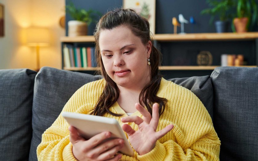 Portrait of young woman with Down syndrome sitting on sofa in living room using tablet