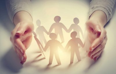 Paper people surrounded by hands in gesture of protection.
