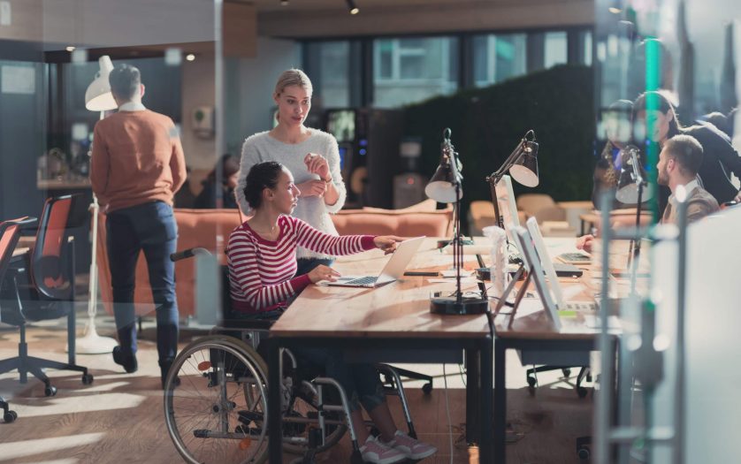Businesswoman in a wheelchair in coworking office space. Colleagues in background.