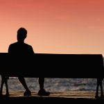 Silhouette of man sitting alone on the bench in front of the sea
