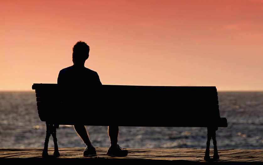 Silhouette of man sitting alone on the bench in front of the sea