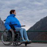 A woman in a wheelchair on a point view admires the high mountains