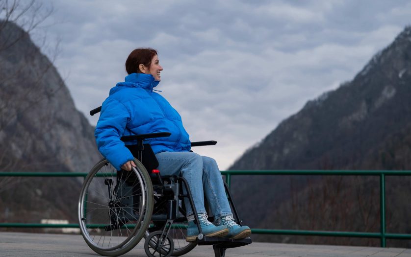 A woman in a wheelchair on a point view admires the high mountains