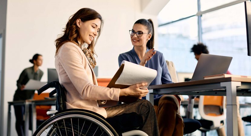 businesswoman in wheelchair going through reports while working female coworker in the office.