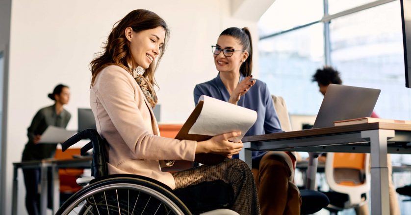 businesswoman in wheelchair going through reports while working female coworker in the office.