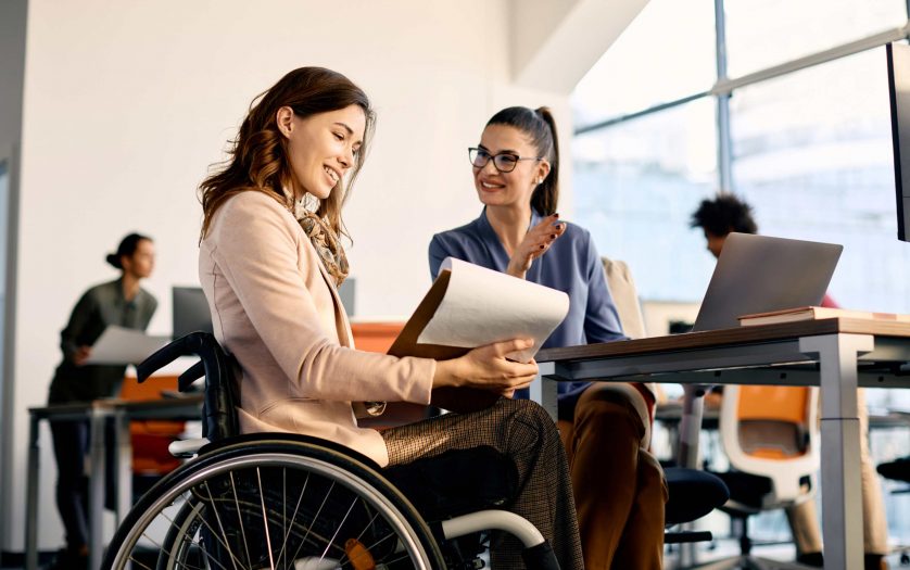 businesswoman in wheelchair going through reports while working female coworker in the office.