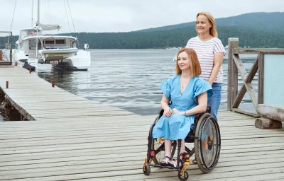 A woman in a wheelchair walks with her sister on a wooden pier by the sea
