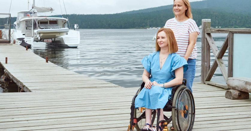 A woman in a wheelchair walks with her sister on a wooden pier by the sea
