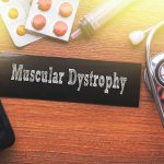 MUSCULAR DYSTROPHY words written on label tag with medicine,syringe,keyboard and stethoscope with wood background