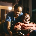 Young female caregiver helping a senior man in a wheelchair in a nursing home at night smiling