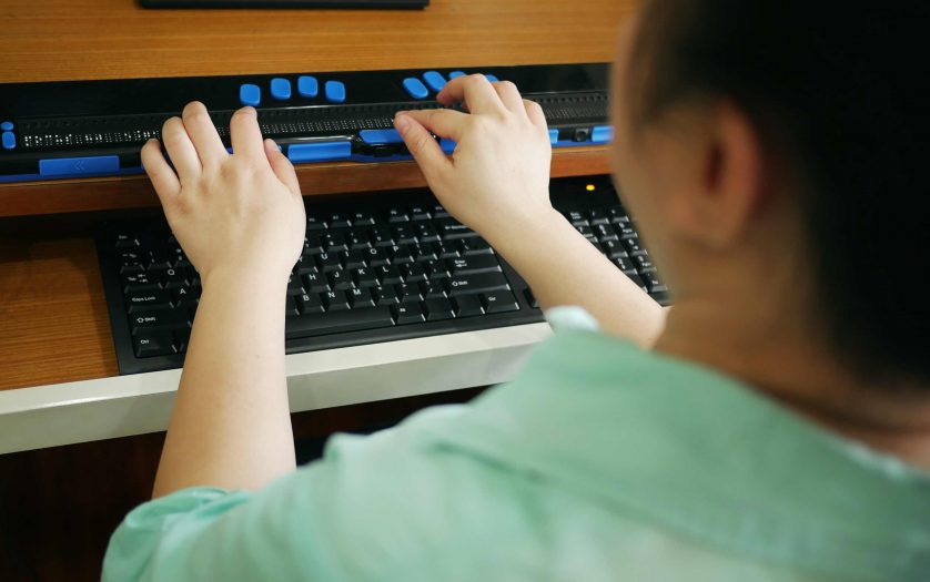 Rear view of person with blindness disability using computer keyboard and braille display
