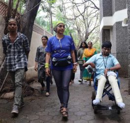 Gita walking with people, in her right side a person in wheelchair