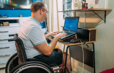 man in wheelchair working on laptop at home.