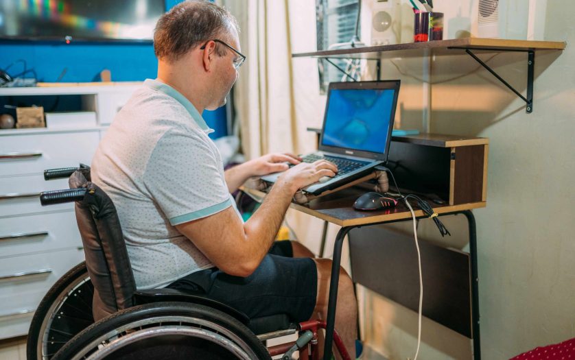 man in wheelchair working on laptop at home.