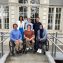 Six athletes, three standing in the back and three in wheelchairs at the front, pose for a photo in front of the IPC headquarters.