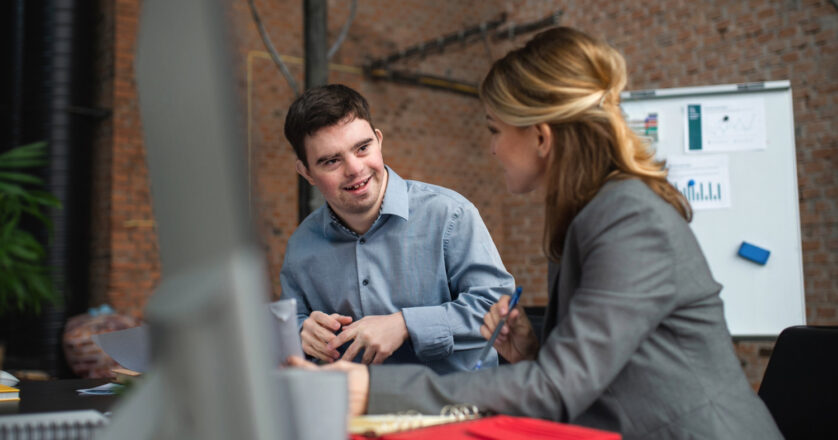Person with Down Syndrome talking with female coworker in the office.