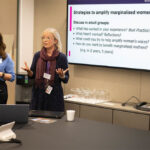 Two woman standing speaking, with a PowerPoint slide visible