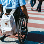 cropped image of man in wheelchair with bag riding on crosswalk