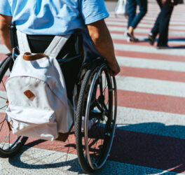 cropped image of man in wheelchair with bag riding on crosswalk