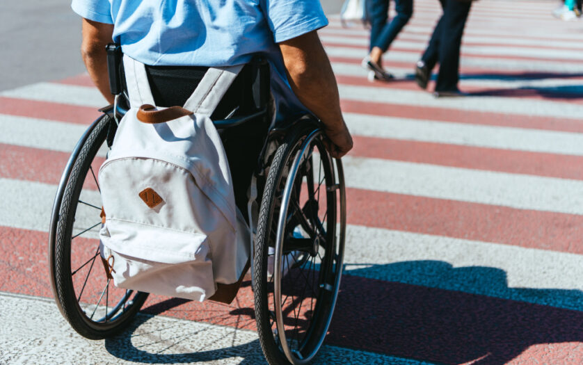 cropped image of man in wheelchair with bag riding on crosswalk