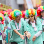 A DeafBlind woman holding hands with her guide, wearing clourful wigs as they dance together during a Kagoshima Ohara Festival.