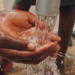 Close-up of a child's hands eshing hands from the spout of a water pump