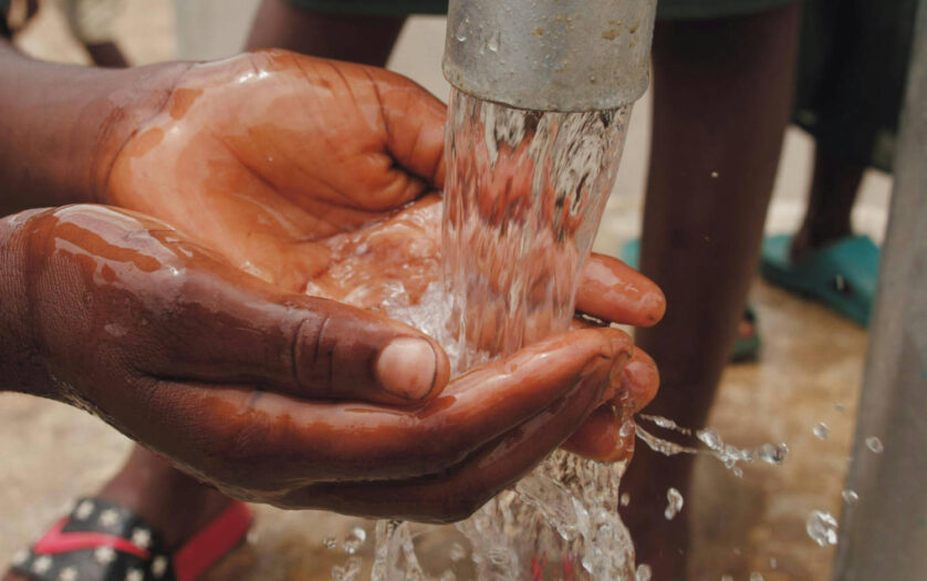 Close-up of a child's hands eshing hands from the spout of a water pump