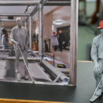 A model of a man with a red had sat on a chair with a white cane next to a photo of a similar figure