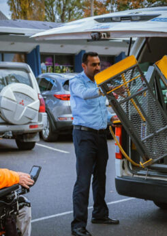 A wheelchair user waits beside a taxi while the driver pulls out the wheelchair lift.