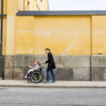 Assistant helping disabled woman in wheelchair move around city